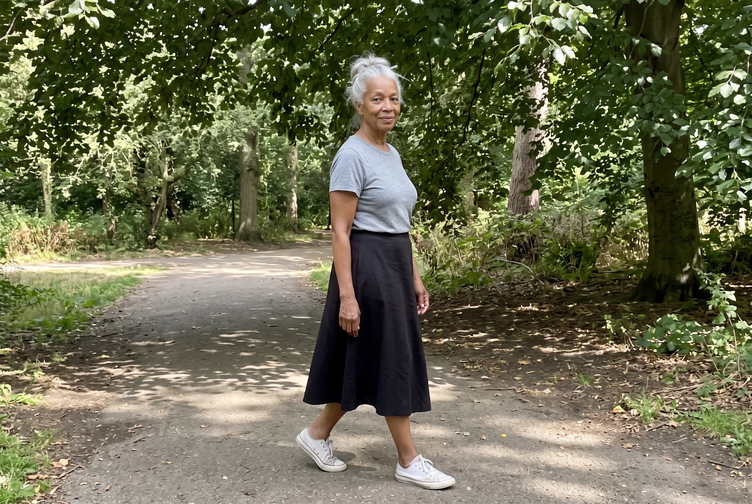 A woman in her sixties walks a park path wearing a gray tee and black skirt.