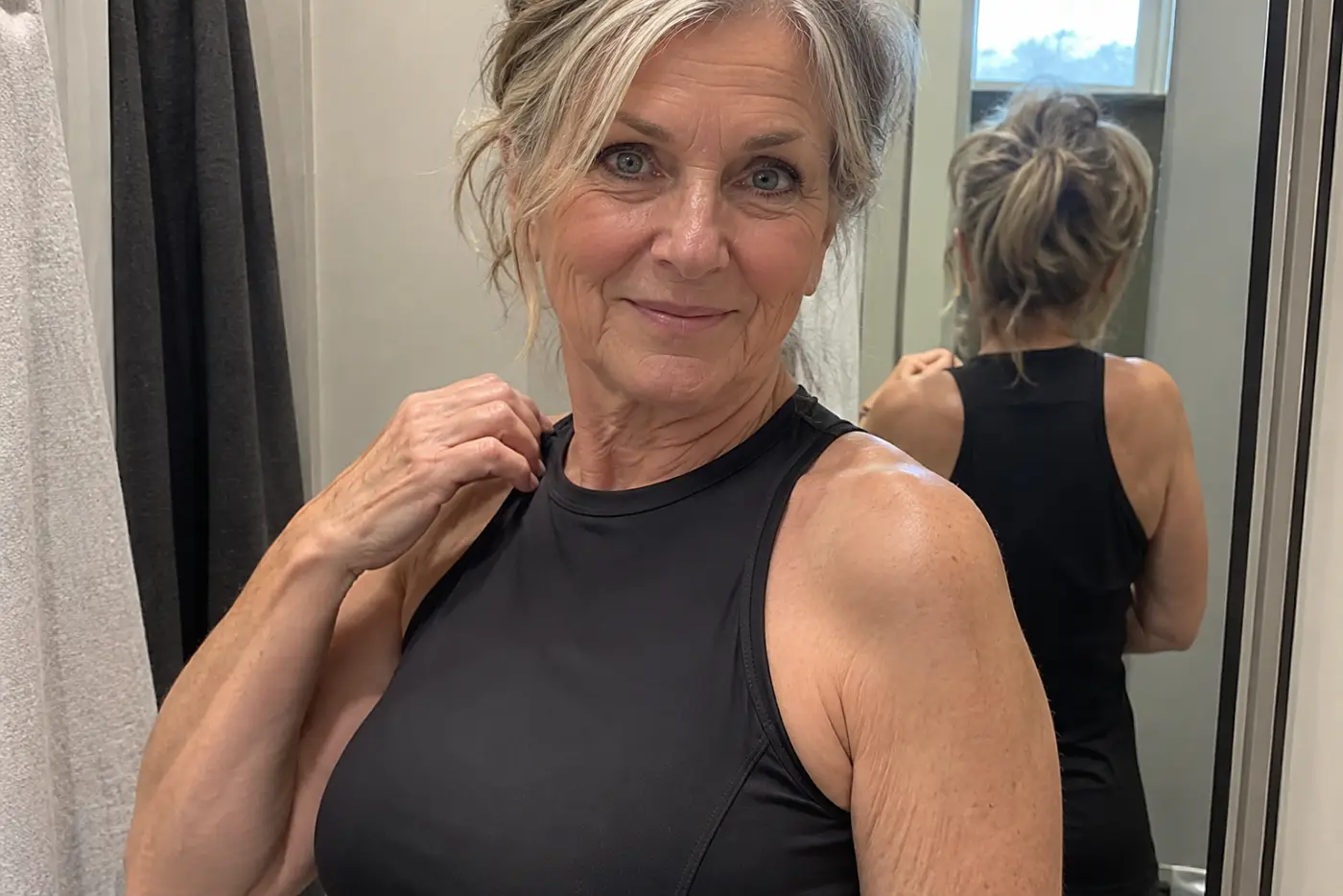 Older woman adjusting a swimsuit strap in a fitting room.