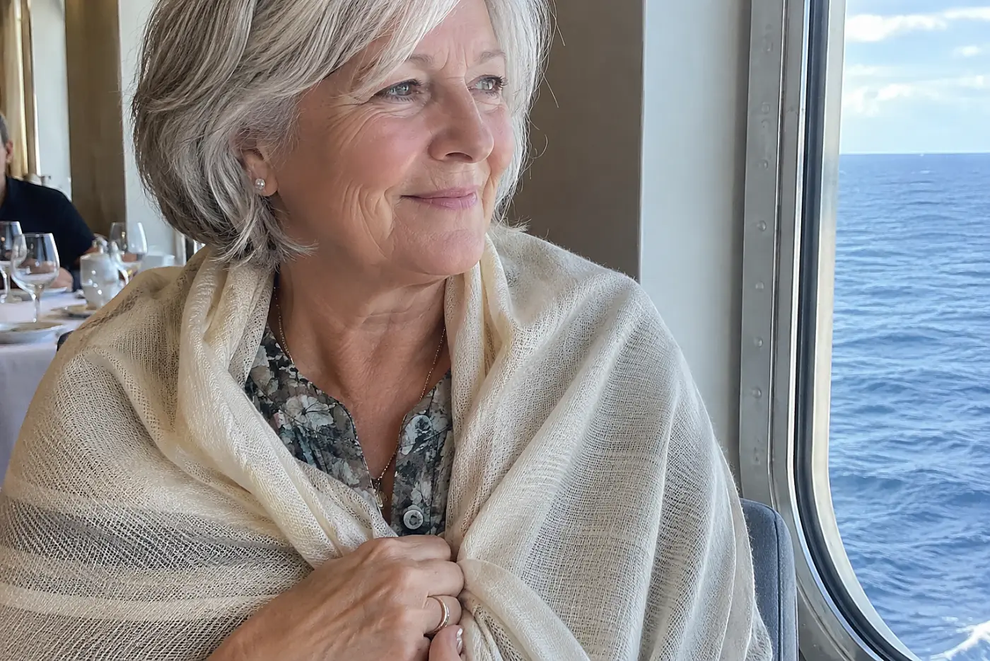 Older woman drawing a light wrap around her shoulders in a ship dining room.