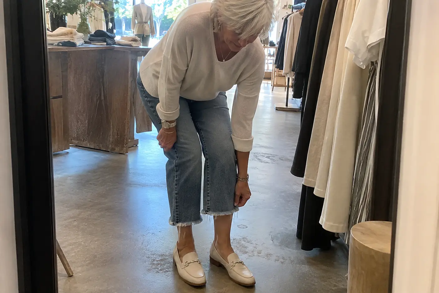 Older woman checking the hem of cropped jeans in a clothing store mirror.