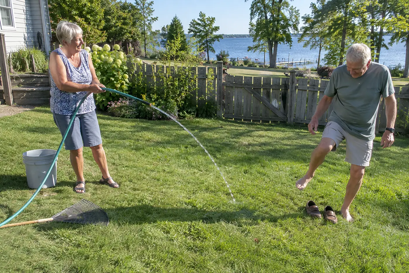 Older woman draining a hose across a backyard lawn.