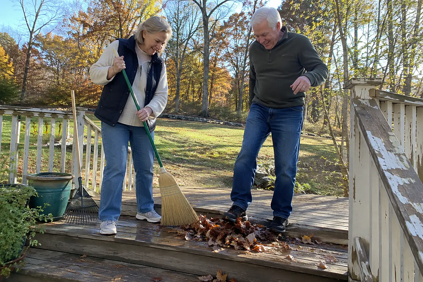 Older woman sweeping wet leaves from deck steps.