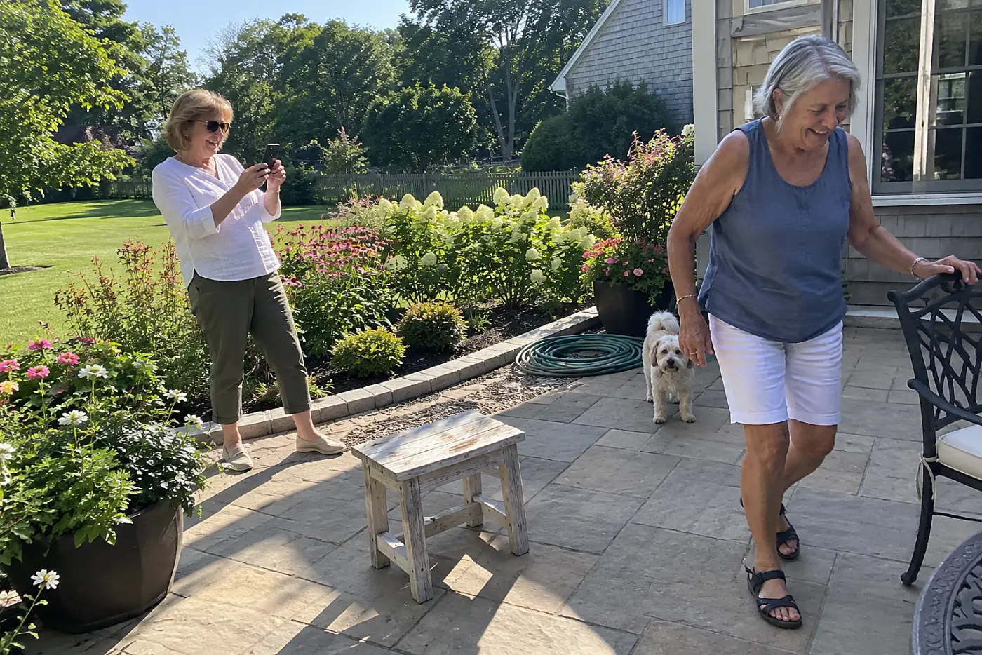 Older woman photographing a garden bed from her patio in afternoon light.