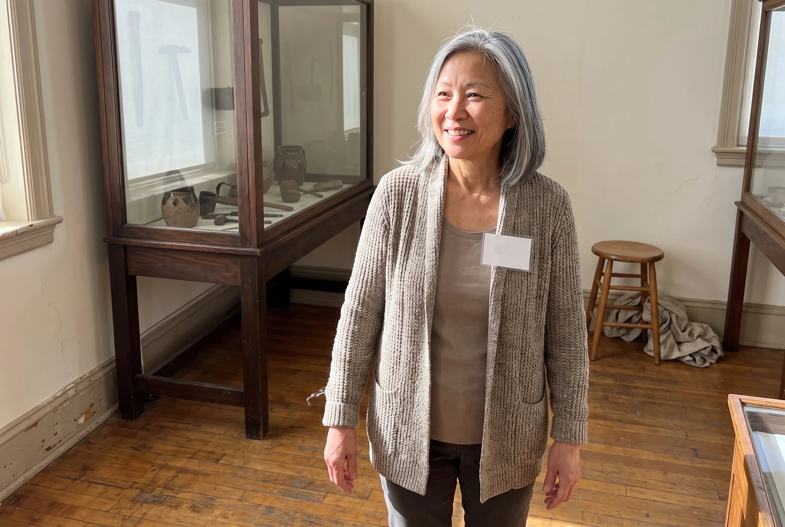 A woman in her sixties welcomes visitors in a local history museum gallery.