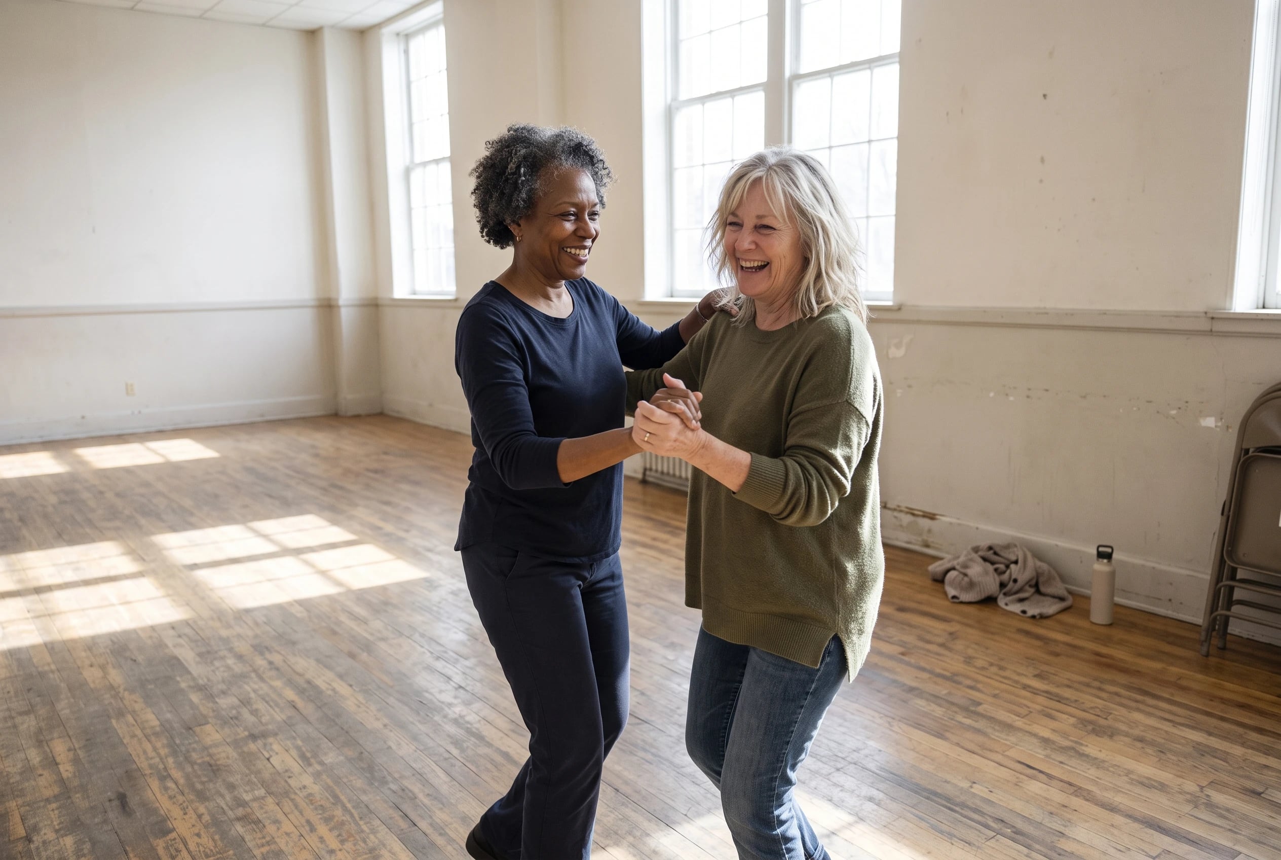 Two women in their sixties practice dance steps at a community center social.