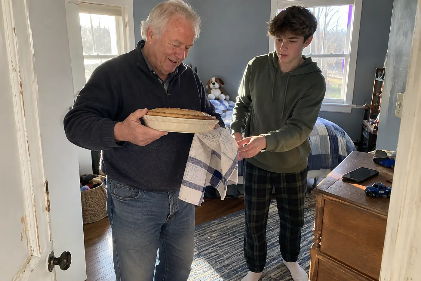 An older woman turns over a ceramic pie dish on her kitchen counter while holding a phone.
