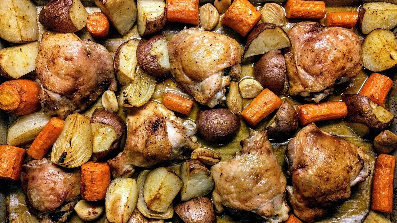 Overhead view of roasted chicken thighs with potatoes, carrots, onions and garlic on a baking sheet