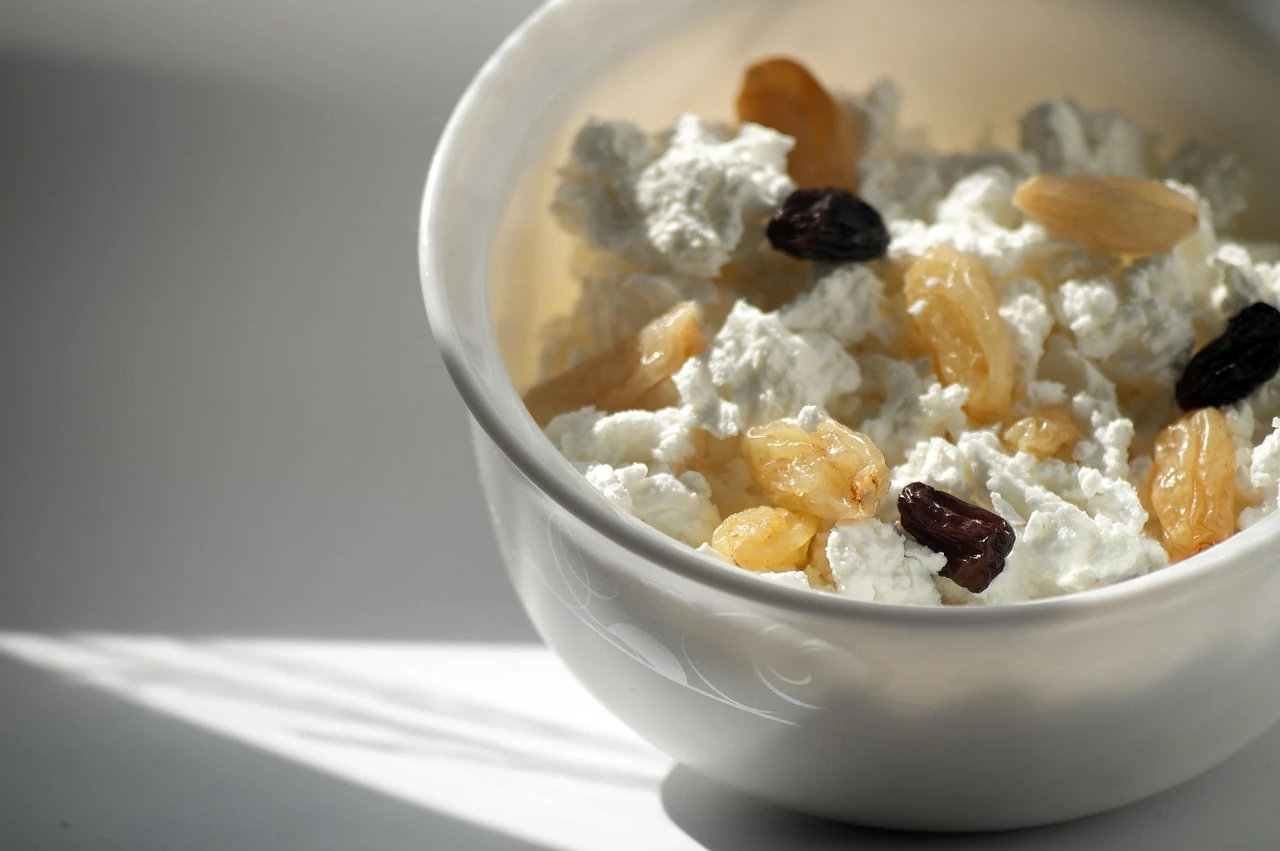 White bowl of cottage cheese topped with golden and dark raisins in soft window sunlight