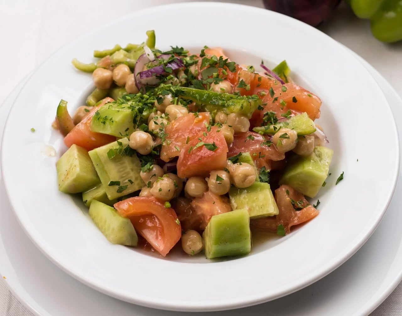 White bowl of chickpea salad with cucumber chunks, tomato, red onion and chopped parsley