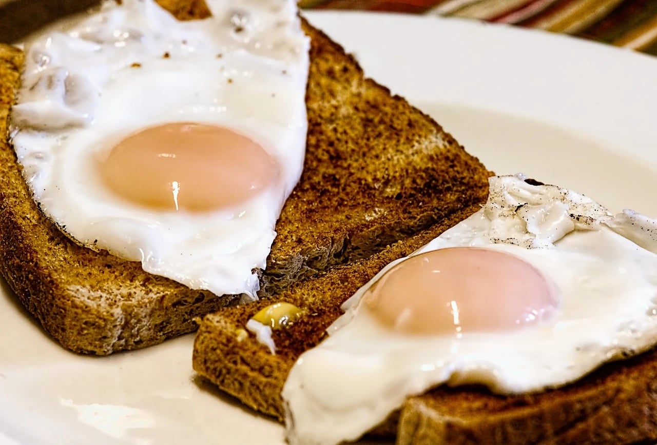 Two sunny-side-up fried eggs resting on slices of toasted bread on a white plate