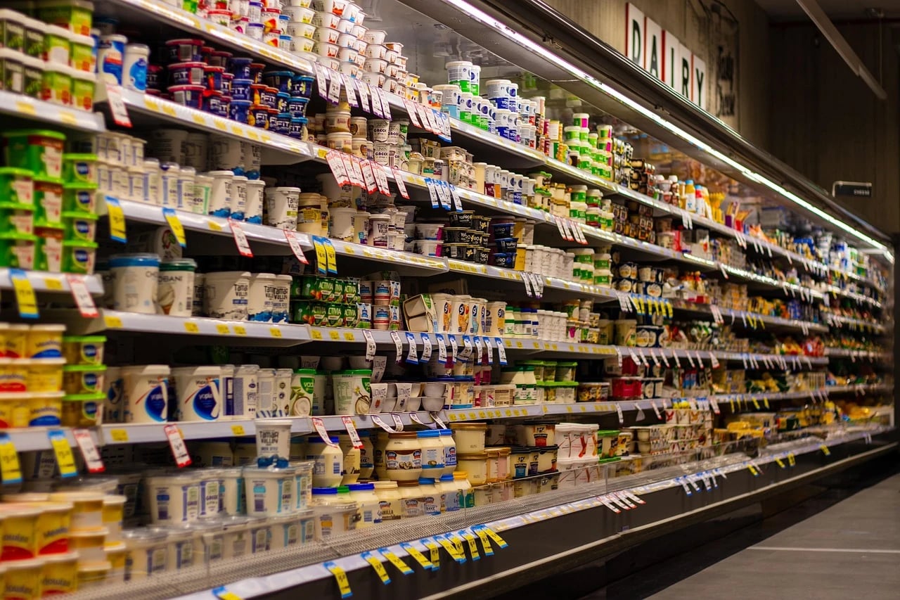 Long supermarket dairy aisle with shelves full of yogurt tubs and cartons under a DAIRY sign