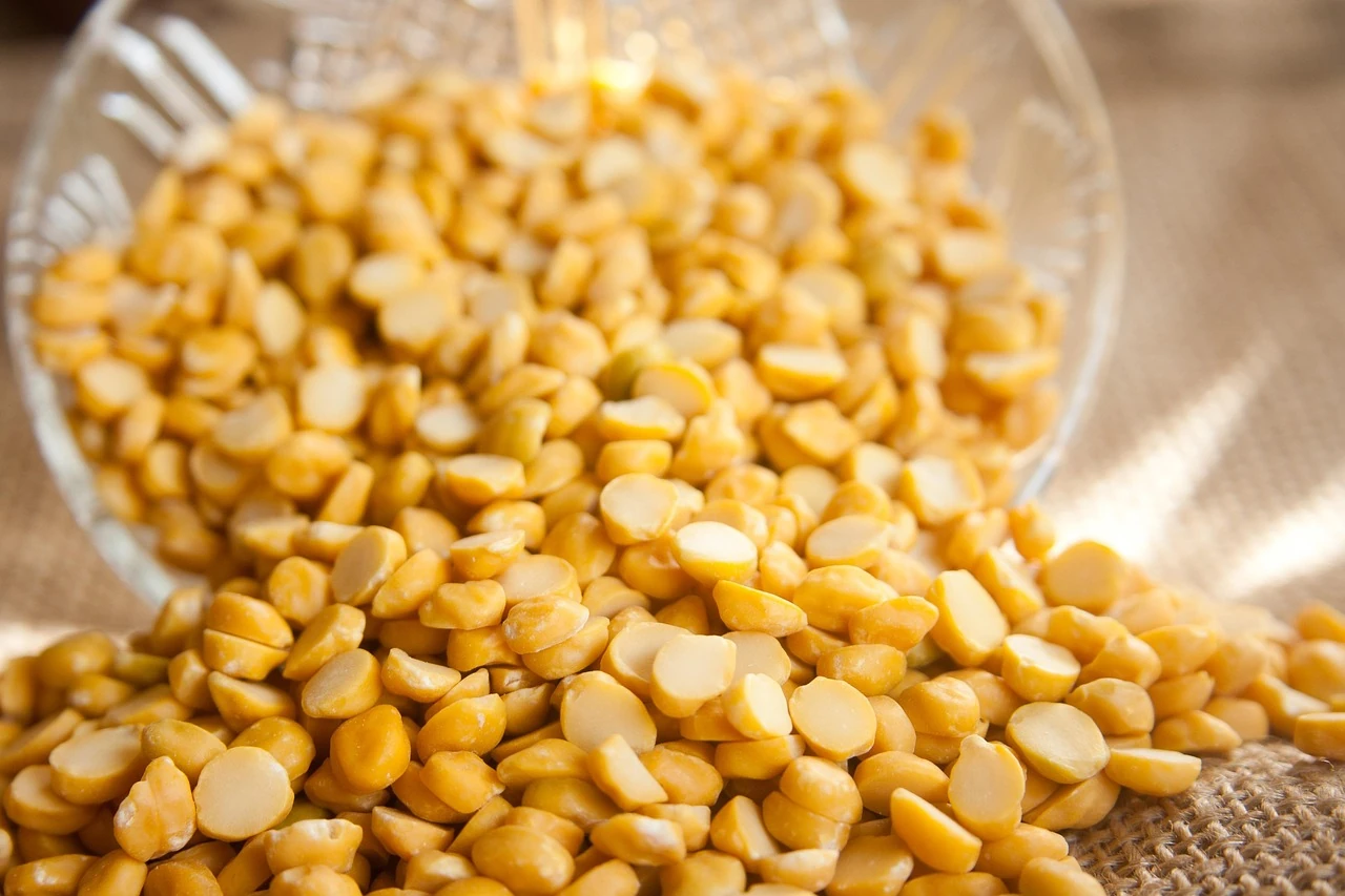 Dried yellow split peas spilling from a glass bowl onto burlap cloth
