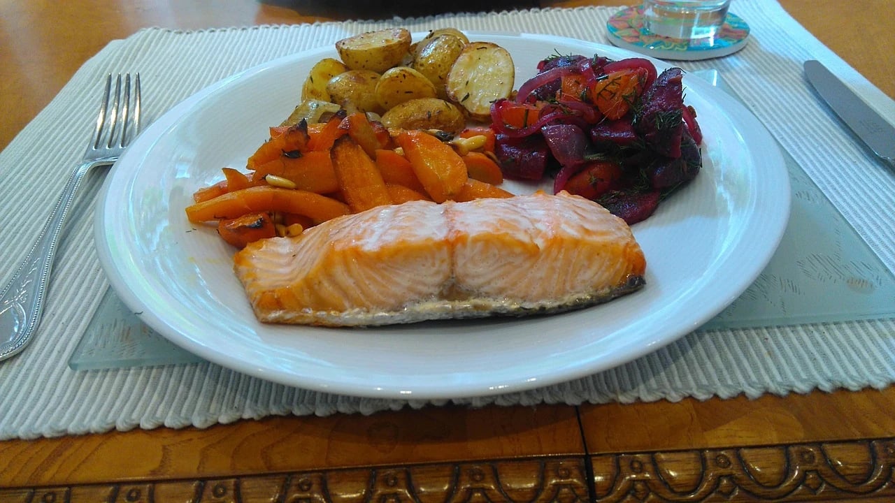 Cooked salmon fillet on a white plate with roasted potatoes, carrots and beet salad on a placemat
