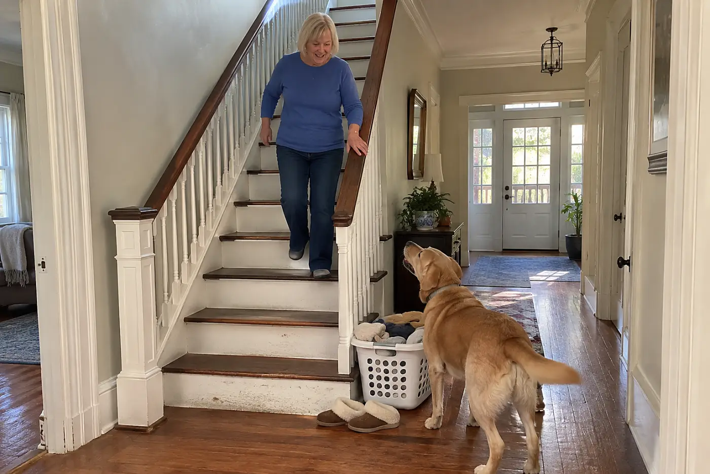 An older woman walks downstairs toward her old dog waiting below.
