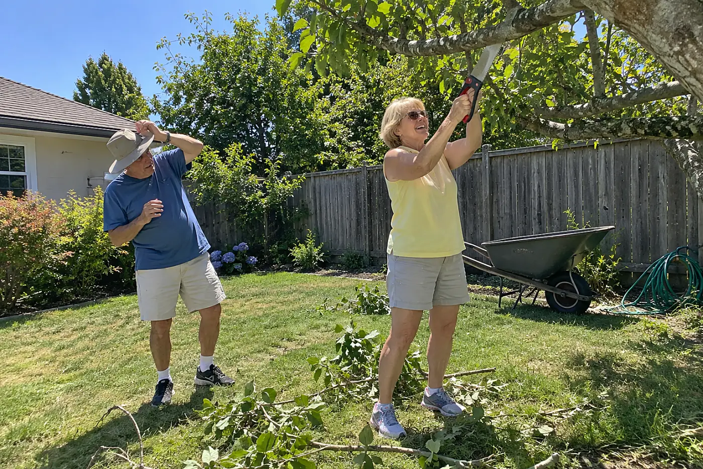 Woman making an underside cut on a large branch in her backyard.
