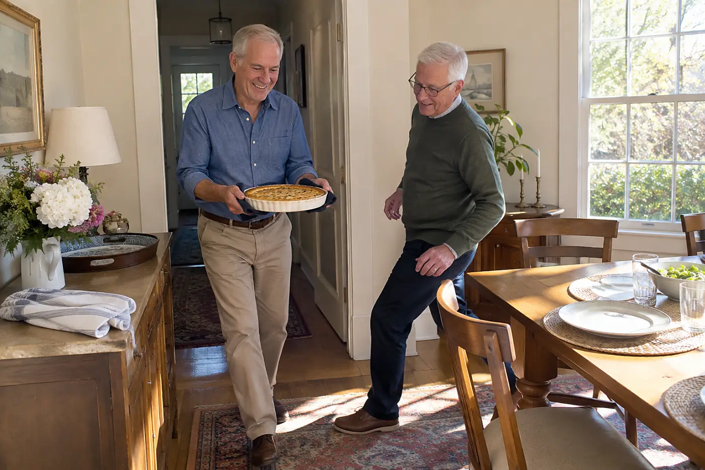 A man carries a baked quiche from a hallway sideboard into a dining room.