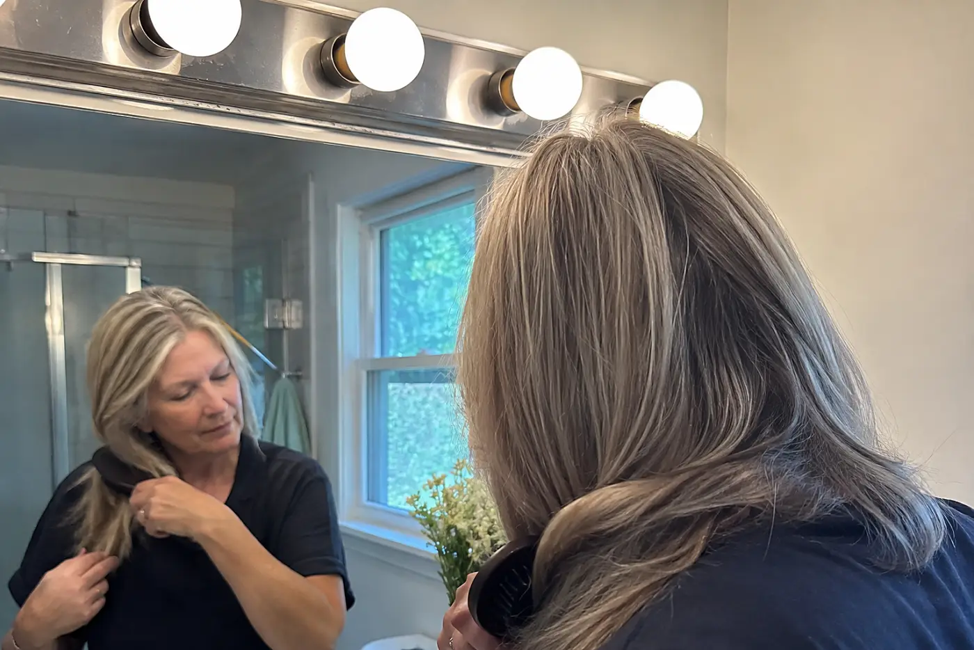 A woman in her sixties brushes her hair beneath a Hollywood vanity light bar.