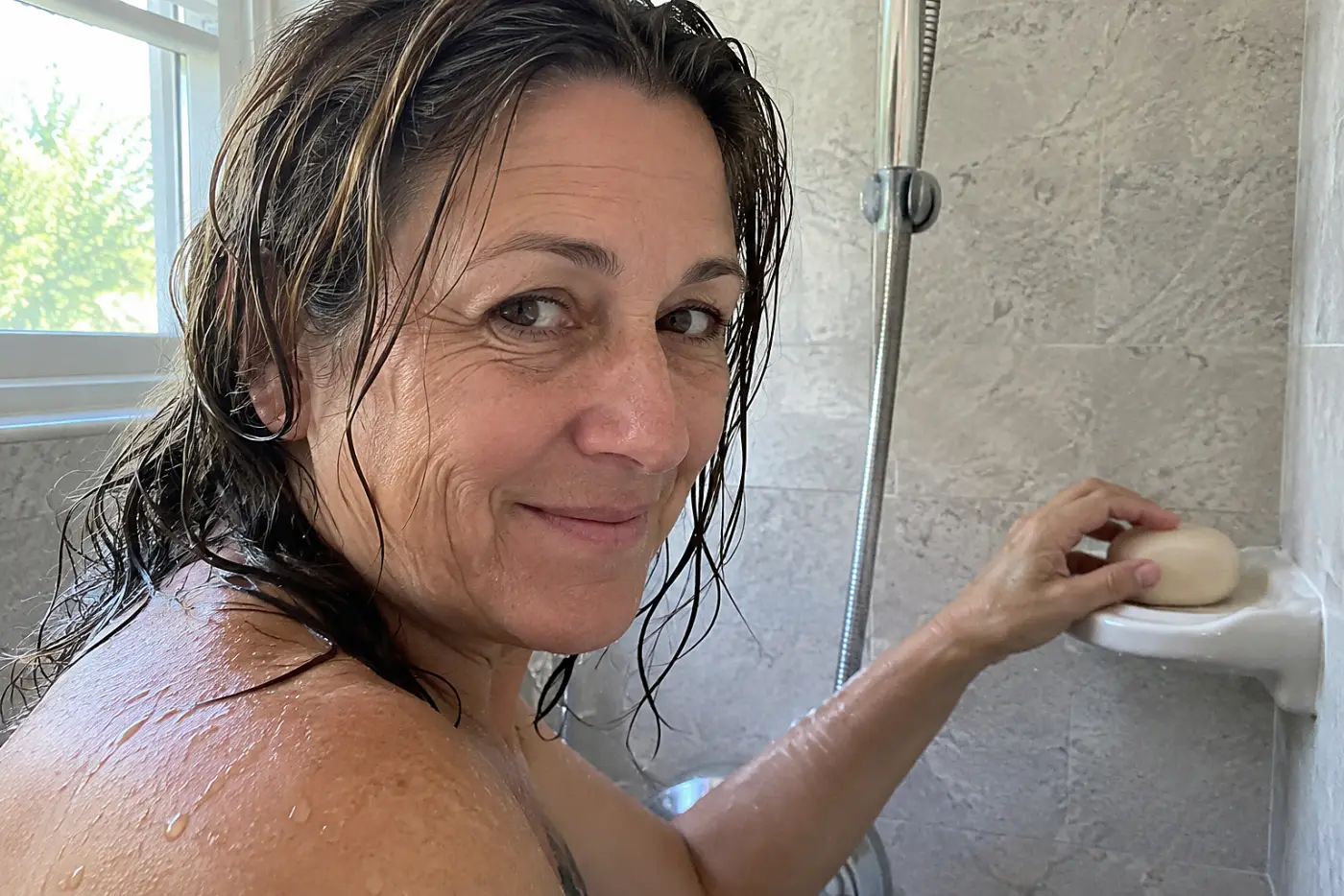An older woman places an Ethique shampoo bar on a soap dish in her shower.