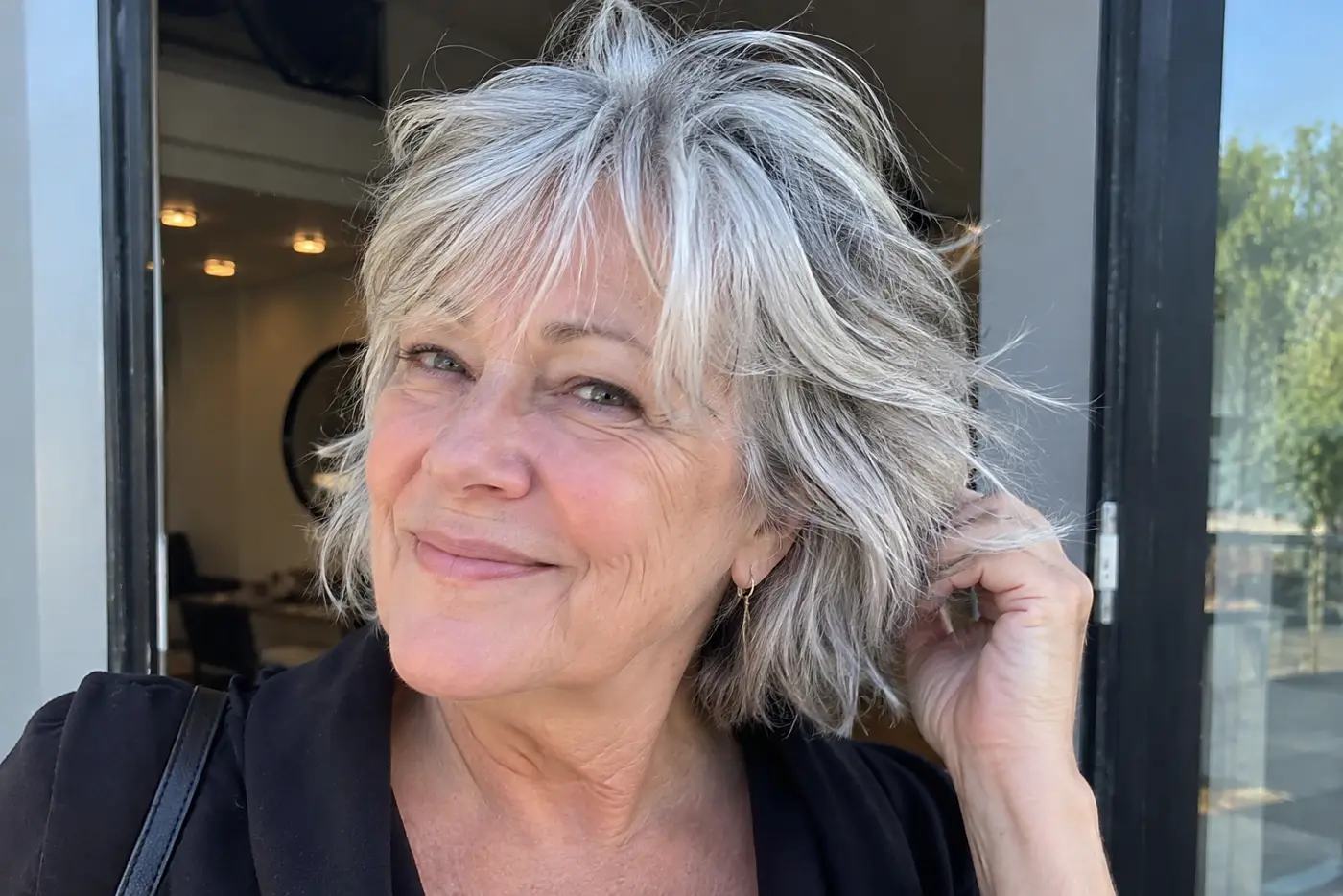 Woman shaking out the layers of her short gray shag outside a salon doorway.