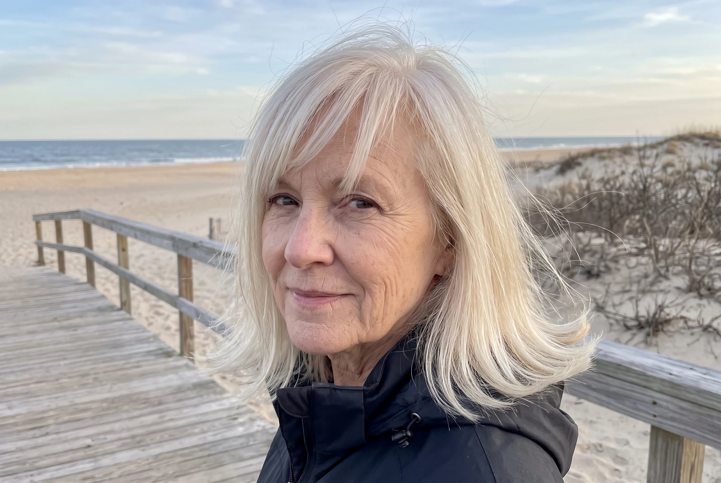 On a boardwalk, a woman in her sixties wears fine blonde hair in a shoulder-length flip.