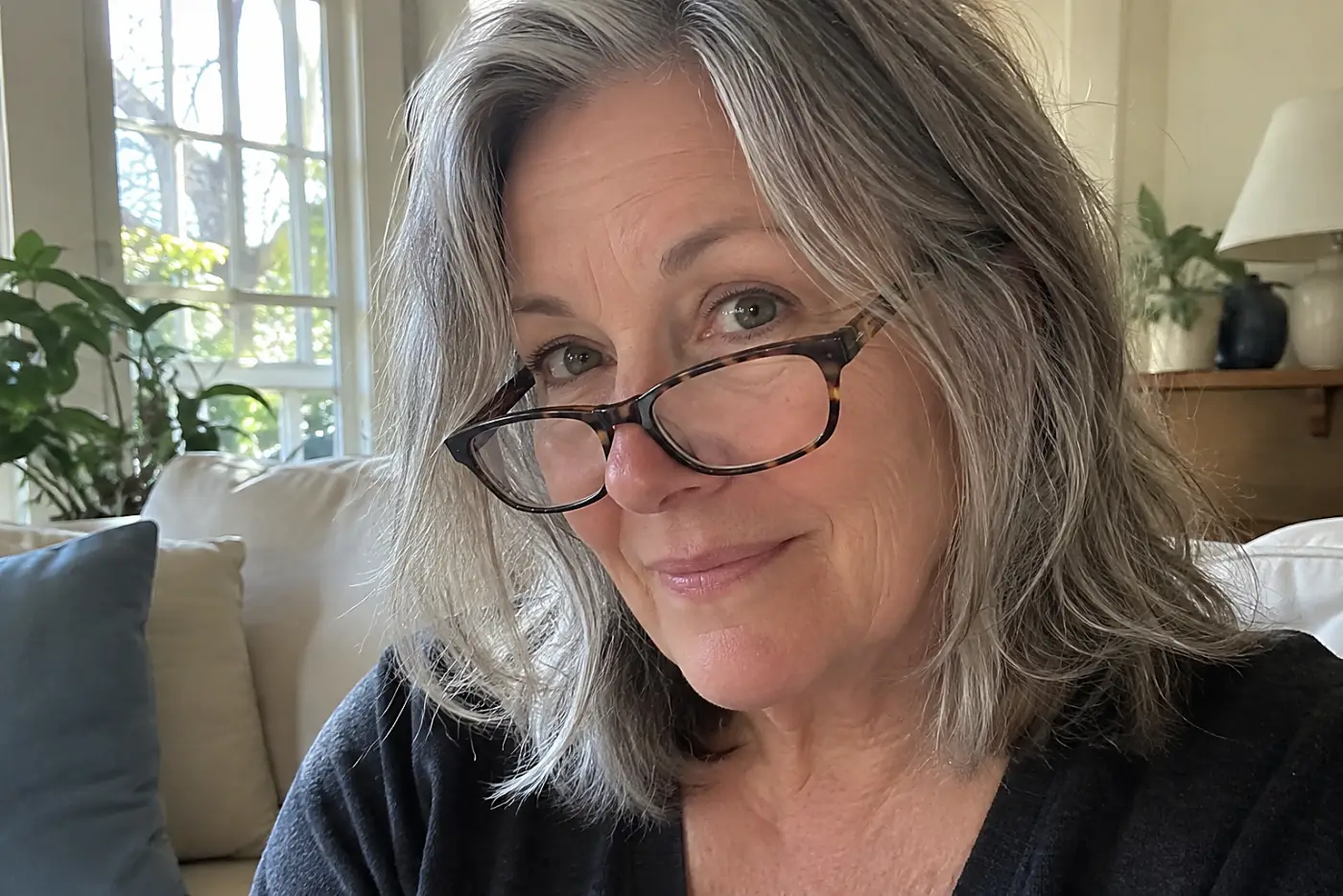 A woman with grey hair wears tortoiseshell glasses that are sliding down her nose.
