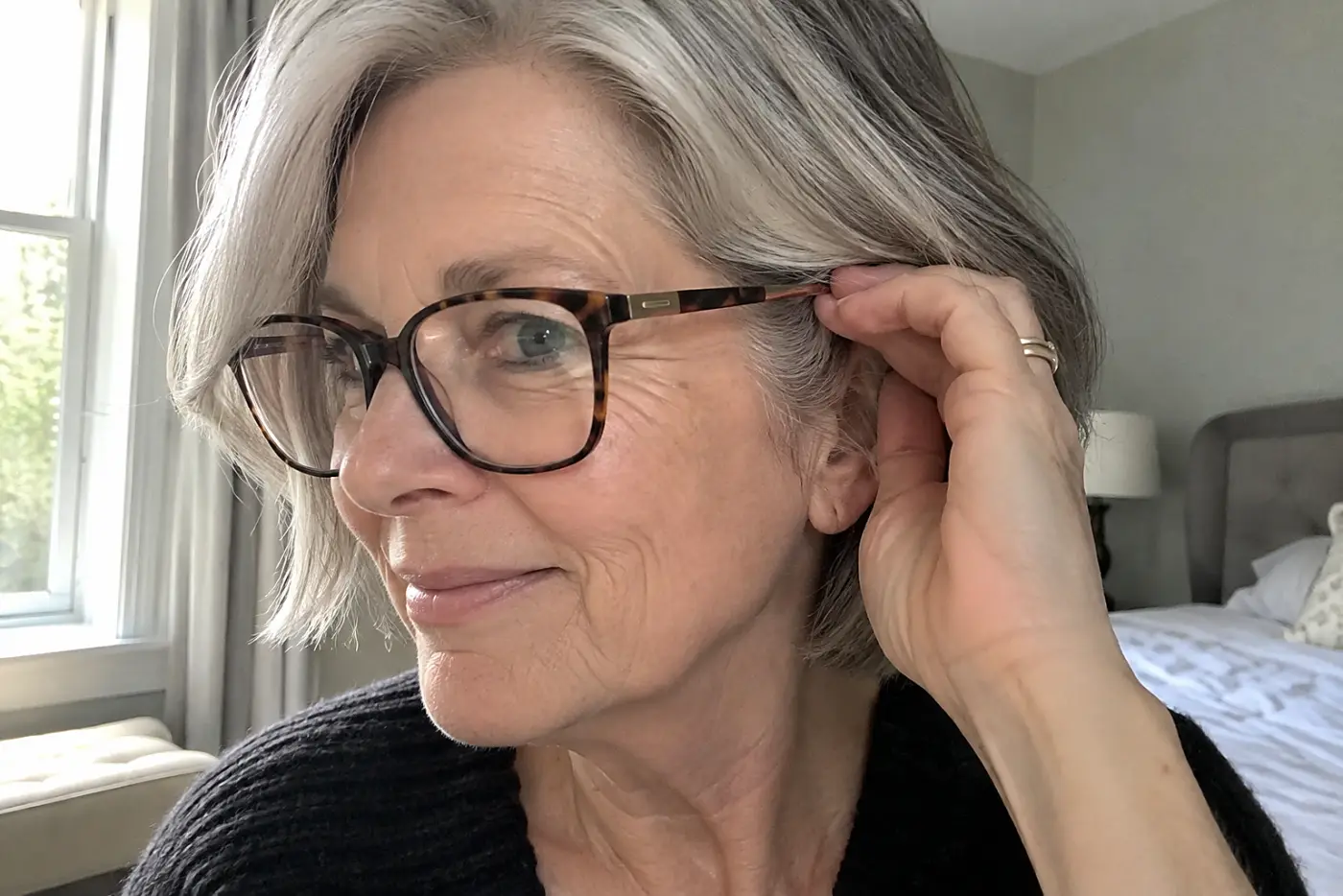 A woman in her sixties with short grey hair adjusts her tortoiseshell glasses frames.