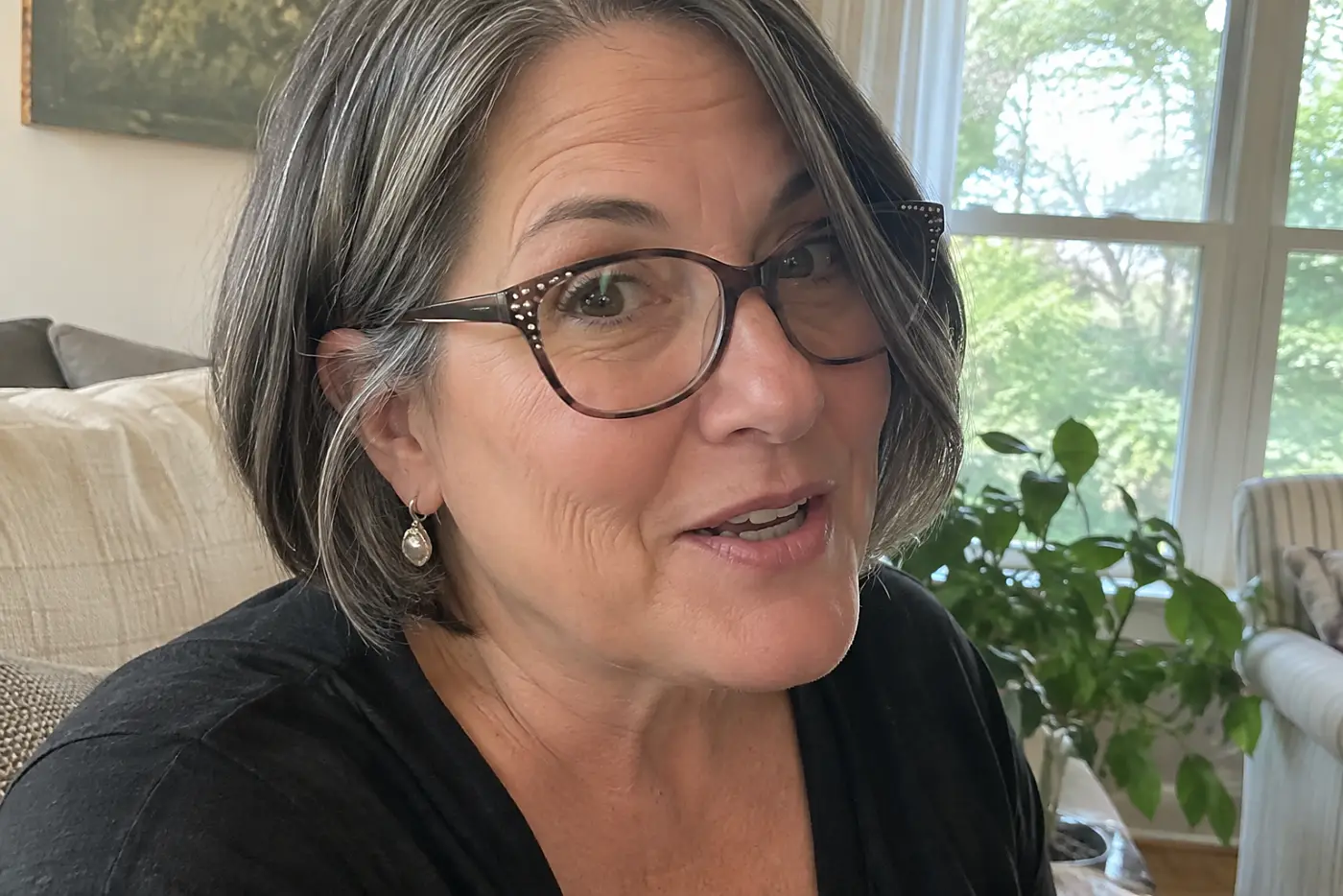 A woman over fifty wearing glasses with rhinestones on the corners talks at home.