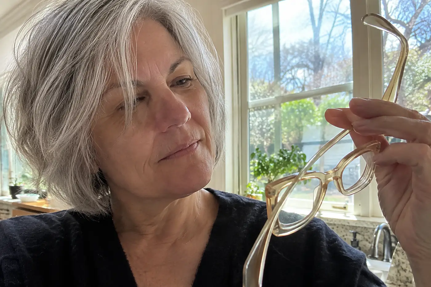 A woman in her sixties with silver hair holds up yellowed clear plastic glasses.