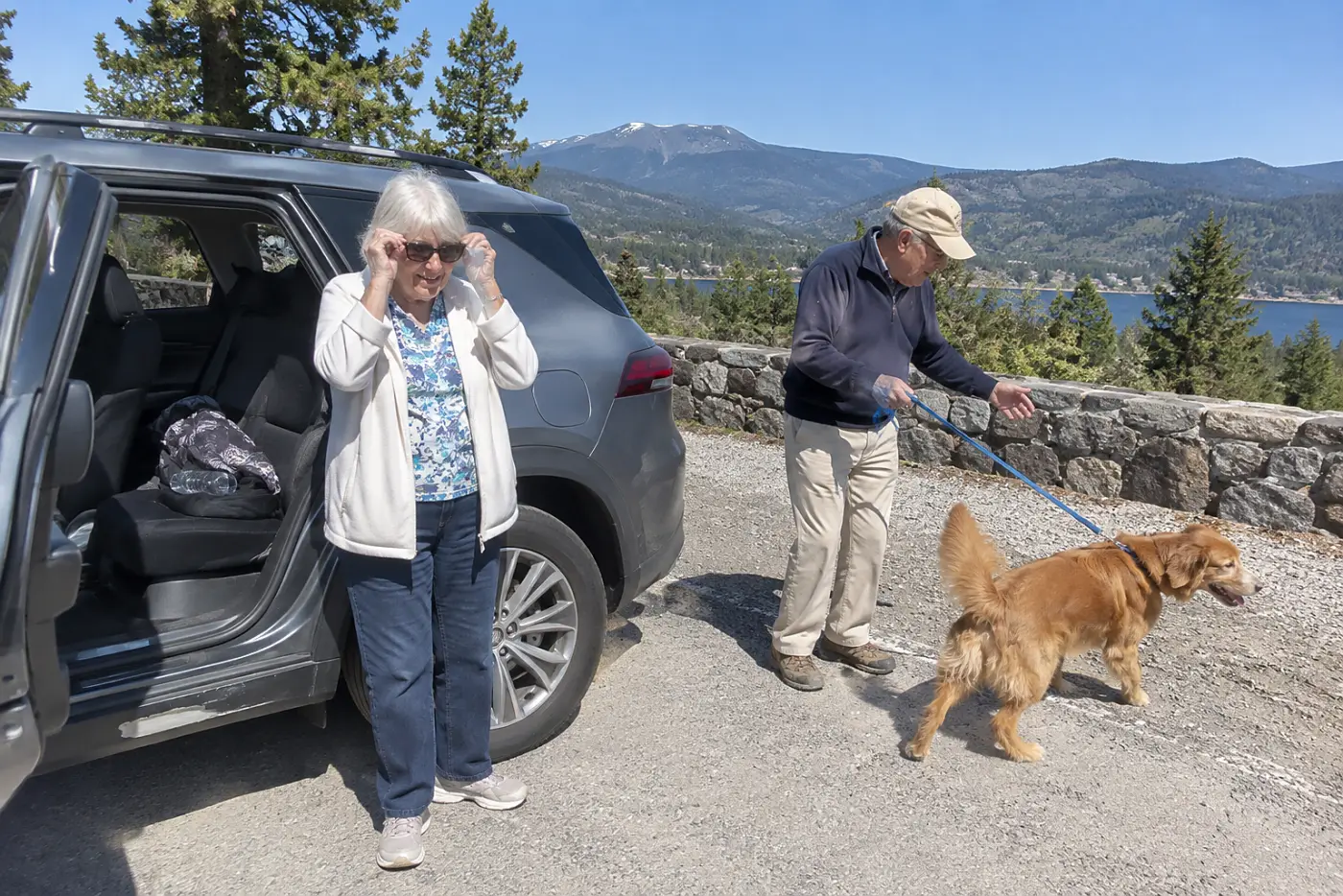 A woman in her seventies adjusts dark clip-on lenses over her glasses beside a car.