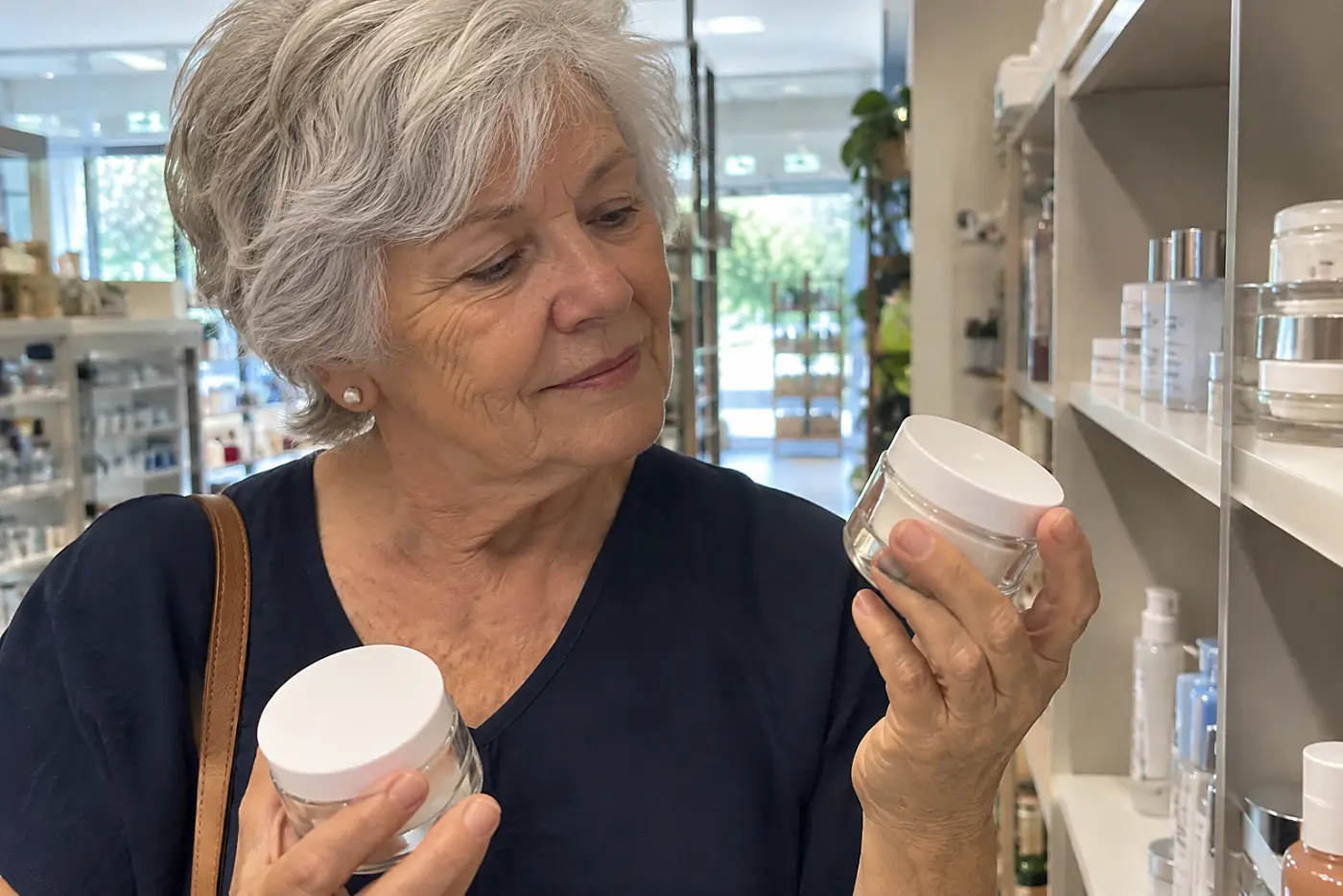 Older woman comparing moisturizer labels in a pharmacy aisle.