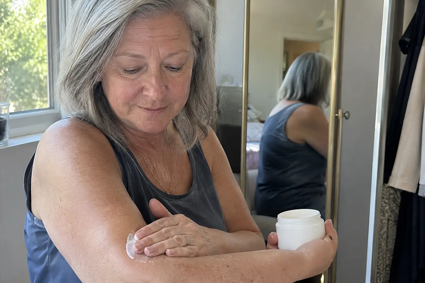 Older woman applying a small dab of cream to her forearm in a dressing room.