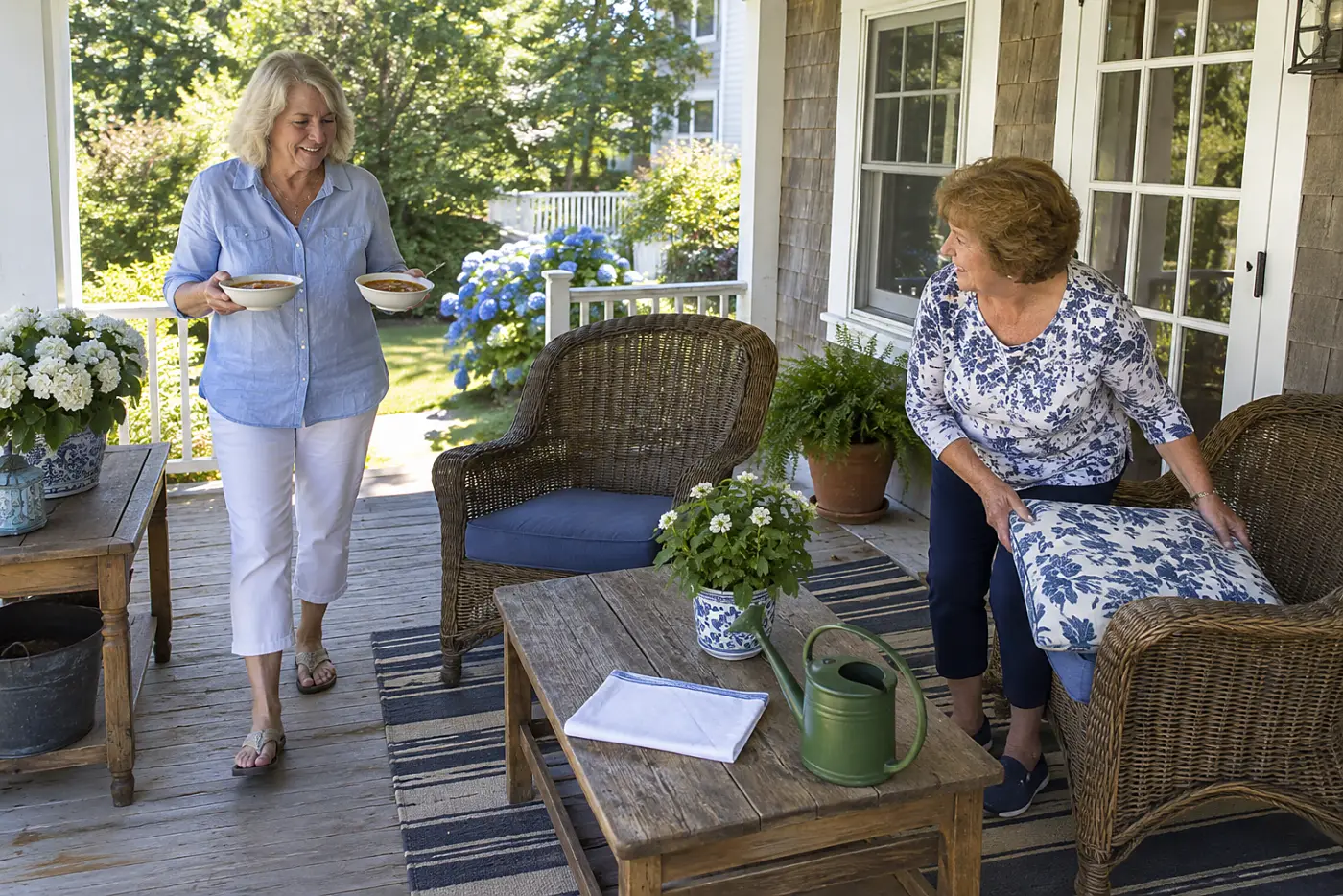 A woman carries two bowls of minestrone from a porch counter toward a pair of chairs.