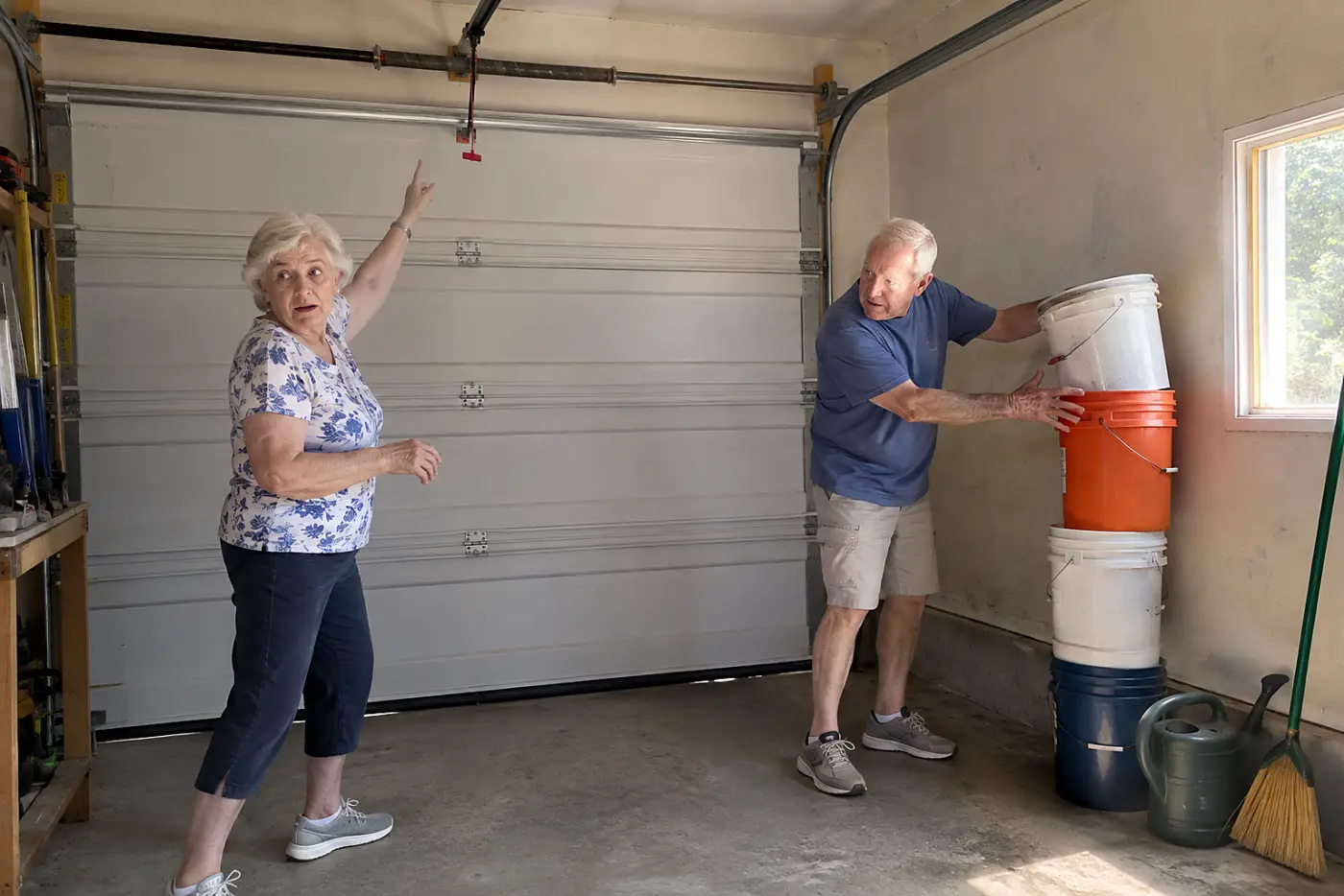 A 72-year-old woman standing inside a garage and pointing out the emergency release handle above a closed garage door.