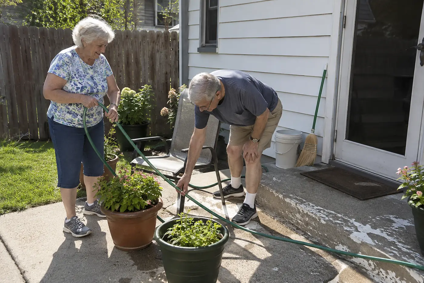 Older woman pulling a hose around two pots beside her back steps.
