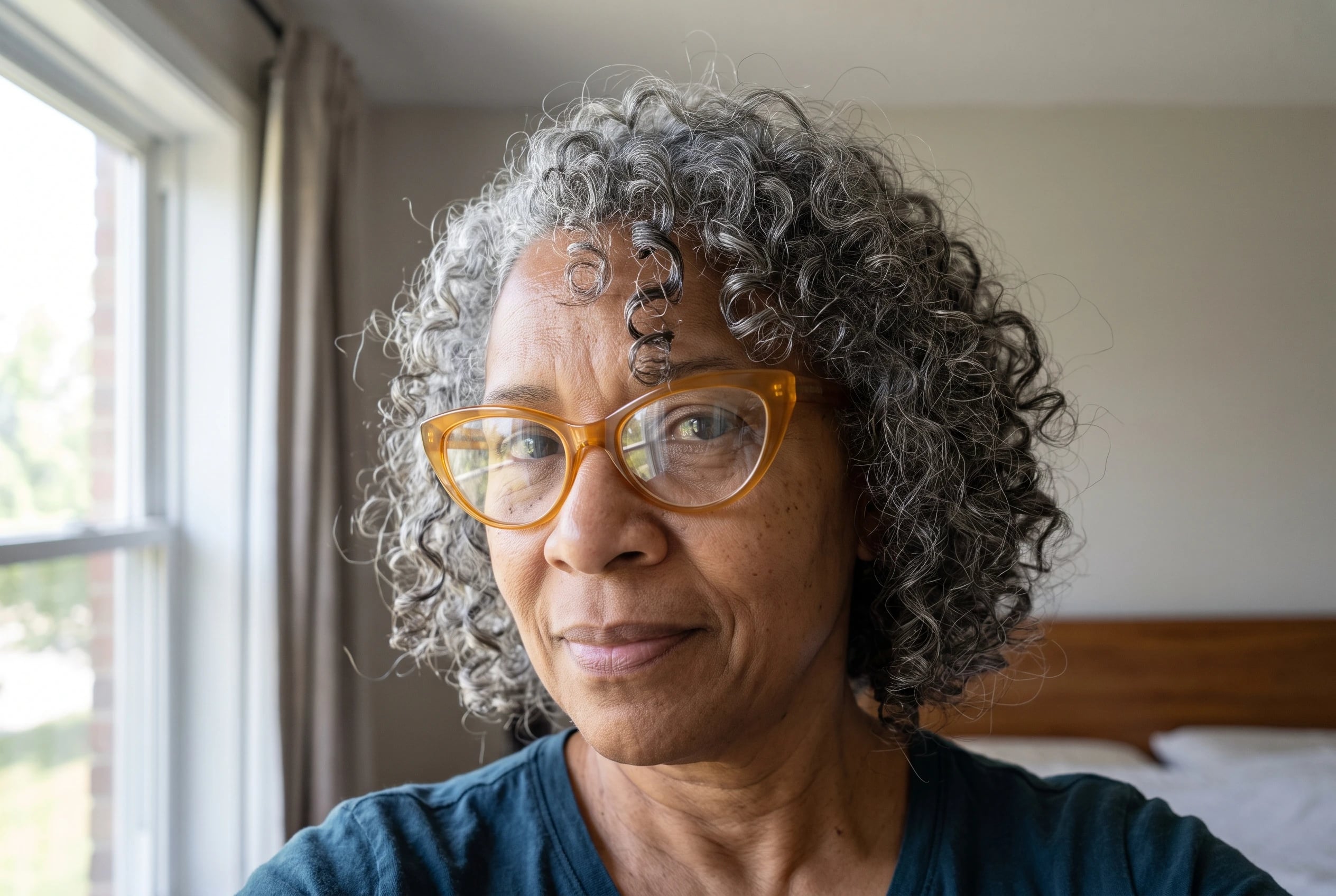 A woman in her sixties with curly gray hair wears amber acetate cat-eye frames.