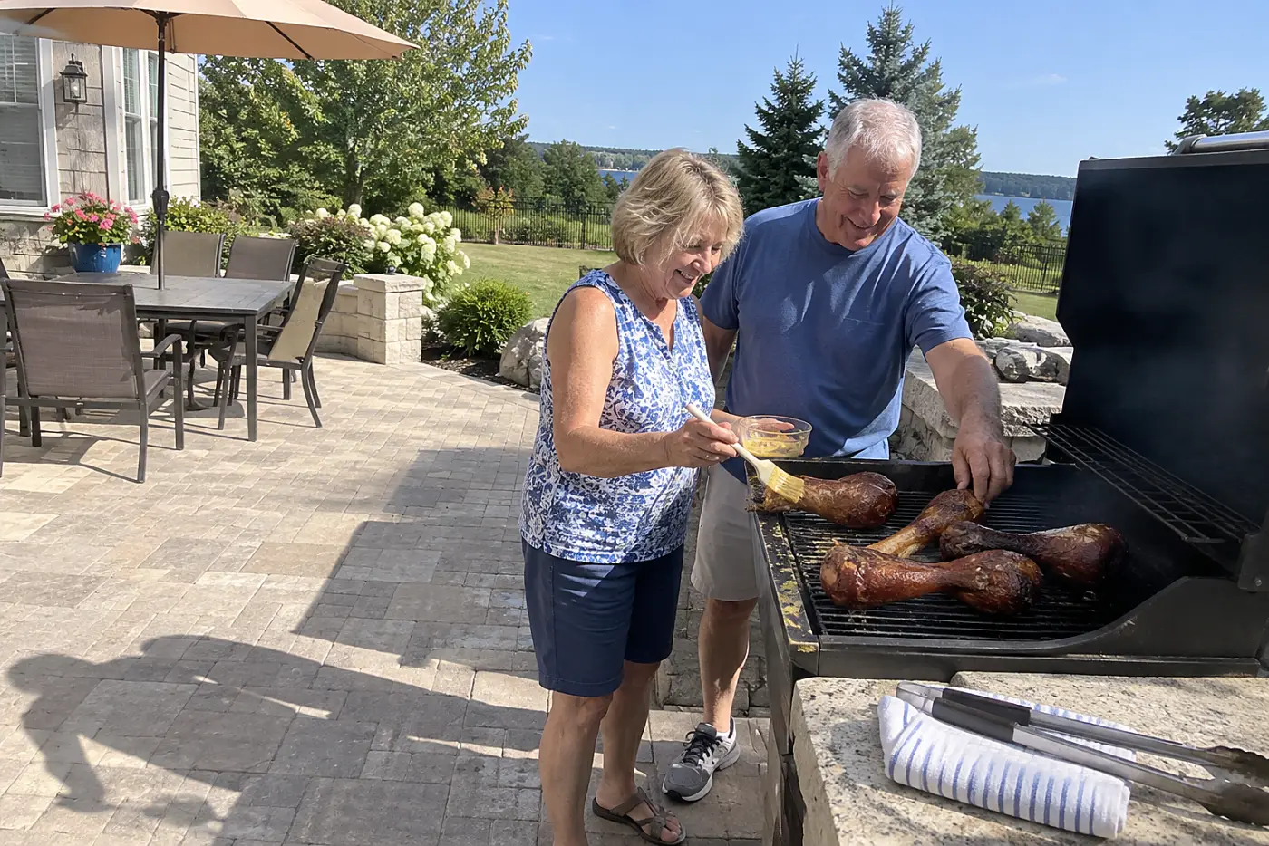 Woman brushes mustard glaze onto smoked turkey legs beside an outdoor grill.