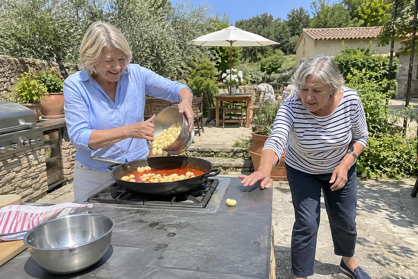 A woman adds gnocchi to tomato sauce at an outdoor cooking station.
