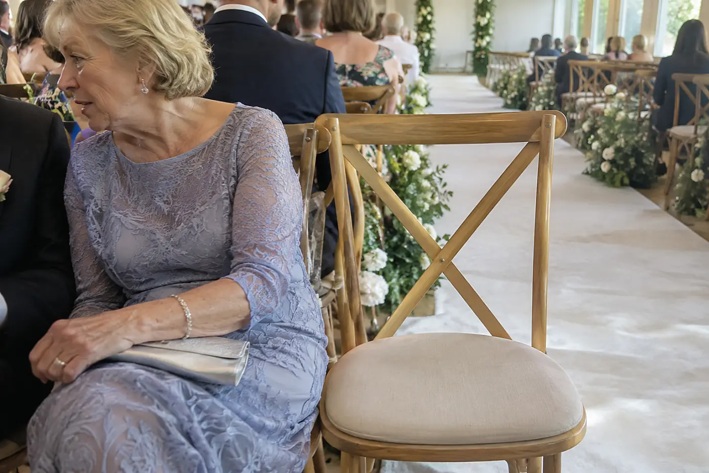 An empty front-row chair sits near a wedding aisle as a woman in her sixties speaks to an usher nearby.