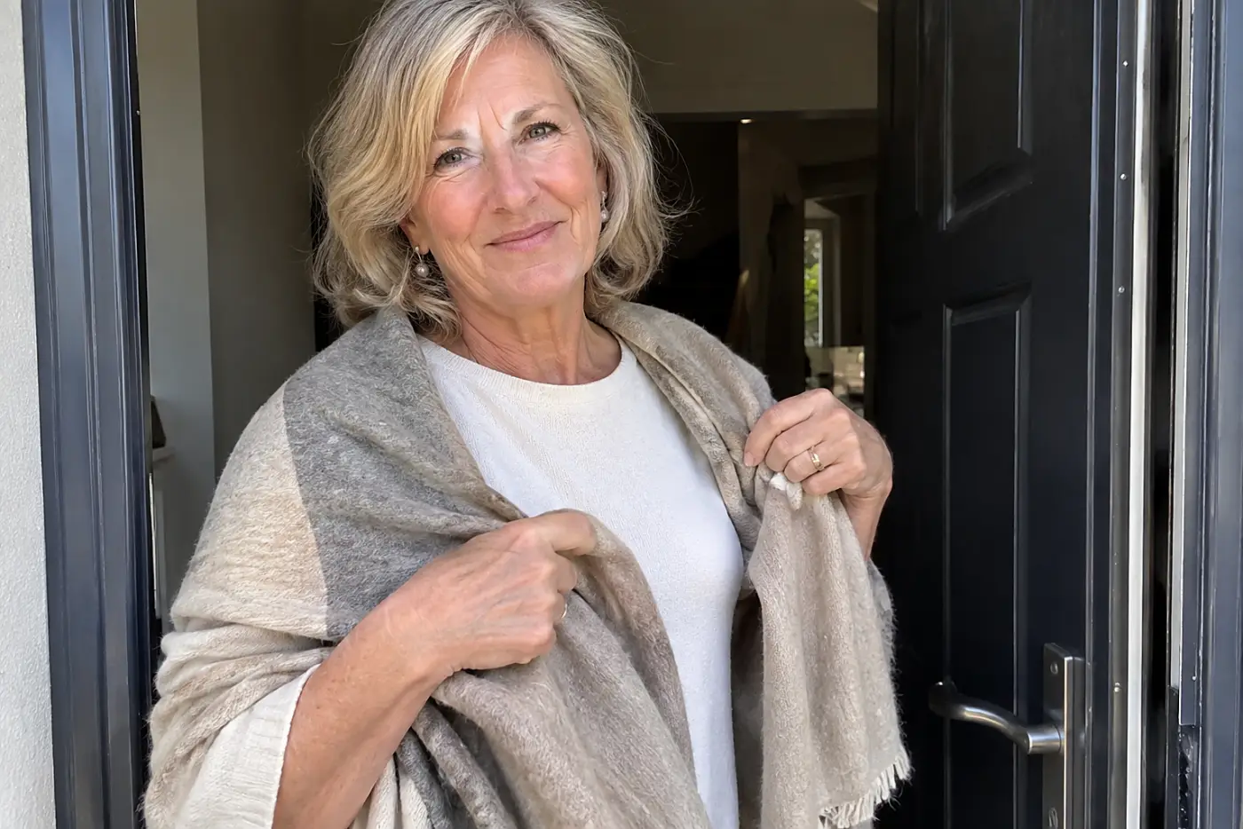 A folded wrap rests in the hands of a woman in her sixties beside the open door of an evening reception.
